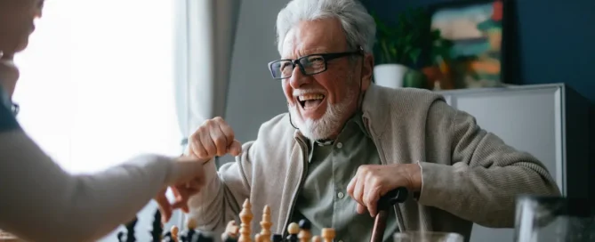 Does playing games help with dementia: senior man laughs while playing chess at a table