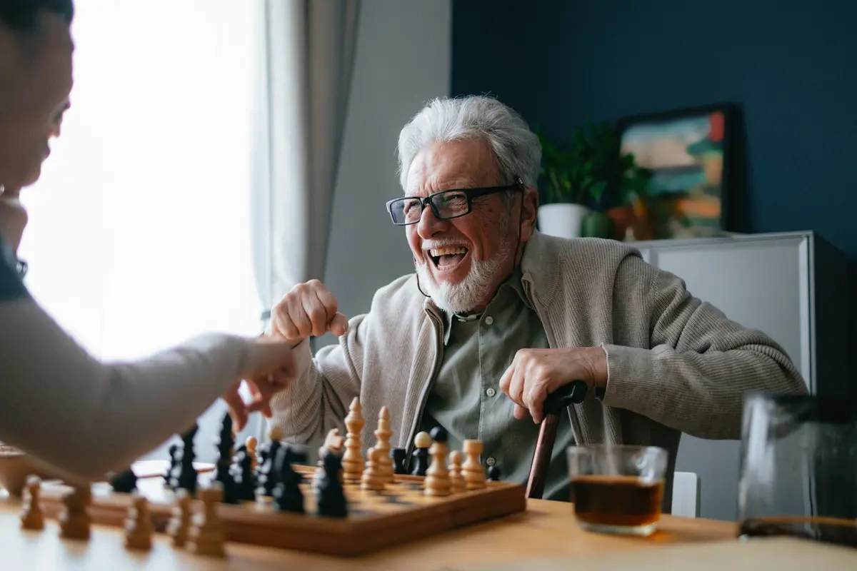 Does playing games help with dementia: senior man laughs while playing chess at a table