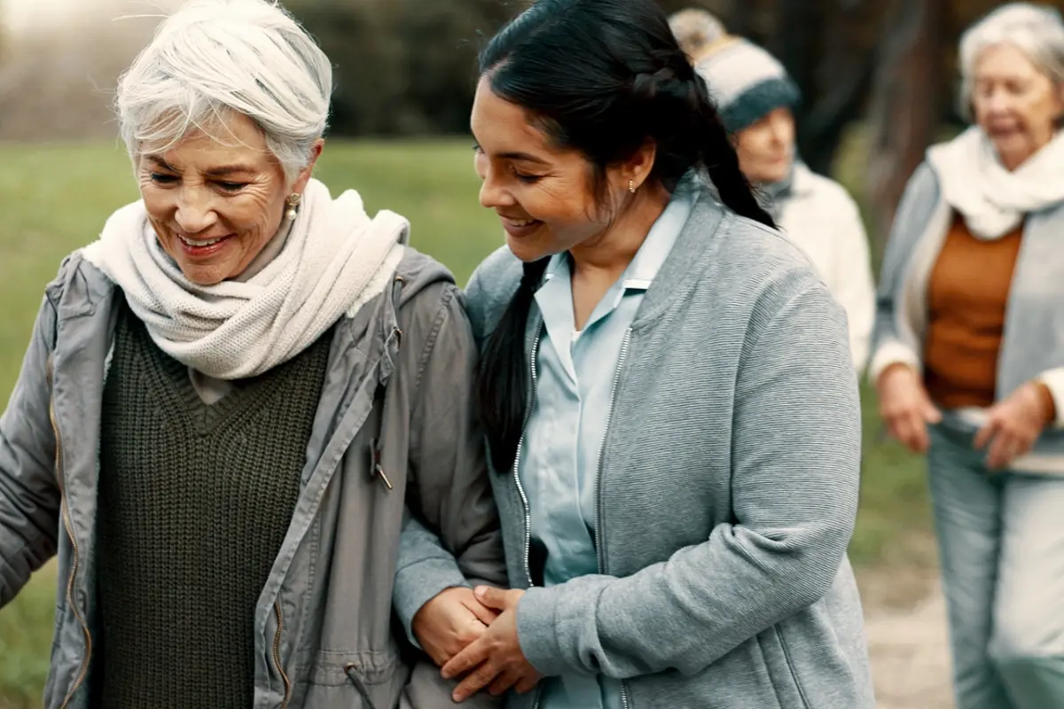 Caregiver challenges: aide supports senior woman during outdoor group walk