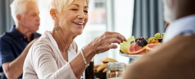 how to help someone with dementia eat shown through an older adult enjoying fruit during a social mealtime.